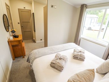 A bedroom with a bed with folded towels on it a desk with a chair and a round mirror on the wall at Sunset Lodge in Woodhall Spa