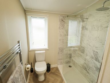 A bathroom with a toilet next to a window and a walk-in shower with marble tiles at Sunset Lodge in Woodhall Spa