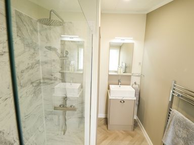 A bathroom with a shower area with marble tiles a small sink with mirror and towel rack at Sunset Lodge in Woodhall Spa
