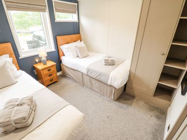 A bedroom with two single beds a wooden nightstand with a lamp and built in shelving at Sunset Lodge in Woodhall Spa