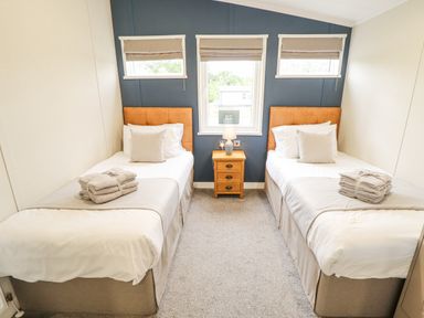A bedroom with two single beds separated by a nightstand with a lamp and three windows at Sunset Lodge in Woodhall Spa