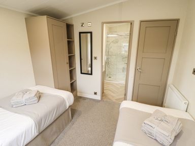 A bedroom with two single beds each with folded towels on them a wardrobe shelves a mirror a door and an entrance to a bathroom at Sunset Lodge in Woodhall Spa