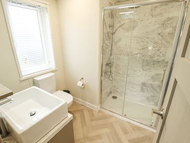 A bathroom with a glass shower enclosure a toilet a sink and a window at Sunset Lodge in Woodhall Spa
