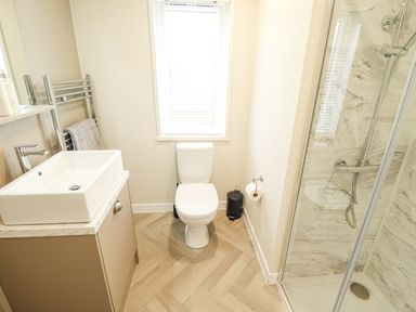 A bathroom with a sink vanity towel rack toilet trash bin and a shower cubicle at Sunset Lodge in Woodhall Spa