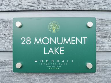 A green sign with the text 28 Monument Lake Woodhall Country Park Lincolnshire on a wooden wall at Sunset Lodge in Woodhall Spa