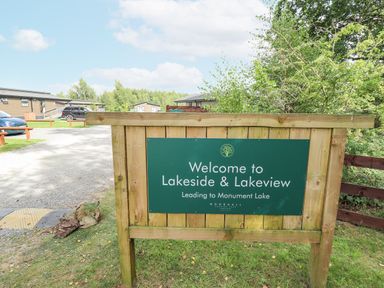 A wooden sign with green background welcoming to Lakeside and Lakeview near parked cars and trees at Sunset Lodge in Woodhall Spa