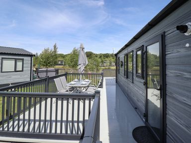 An outdoor deck with a dining table and chairs next to a cabin at Sunset Lodge in Woodhall Spa