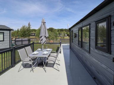 An outdoor deck with a dining table set with plates and glasses next to a building at Sunset Lodge in Woodhall Spa