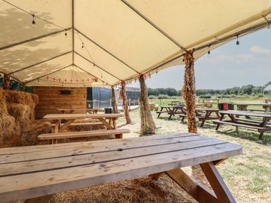 An outdoor seating area with wooden picnic tables under a tent near hay bales at Sunset Lodge in Woodhall Spa