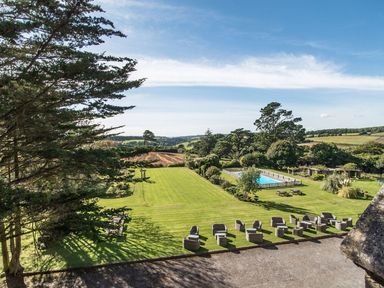 An outdoor area with lawn chairs tables a swimming pool and trees at Alston Hall in Battisborough Cross