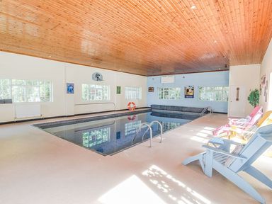 An indoor swimming pool with colorful chairs along one side and a wooden ceiling at Alston Hall in Battisborough Cross