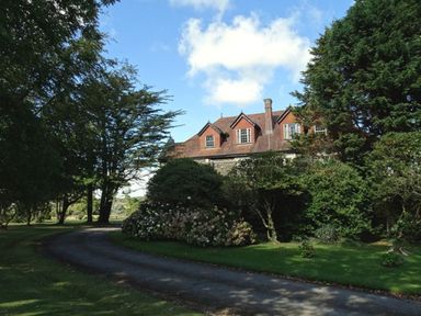A country house with dormer windows surrounded by trees and bushes along a curved driveway at Alston Hall in Battisborough Cross