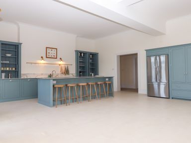 A kitchen with blue cabinets a stainless steel refrigerator a marble countertop and wooden stools at Alston Hall in Battisborough Cross
