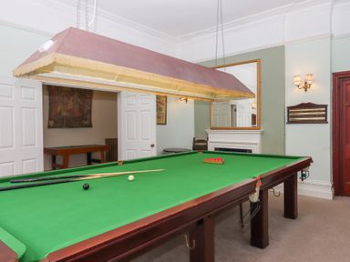 A billiards room with a pool table cues balls light fixture and wall mirror at Alston Hall in Battisborough Cross
