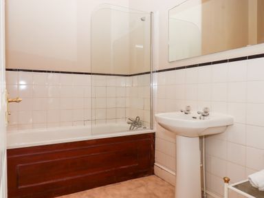 A bathroom with a bathtub glass shower screen tiled walls and a pedestal sink at Alston Hall in Battisborough Cross