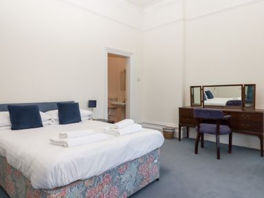 A bedroom with a bed with blue pillows and white towels and a wooden dresser with a mirror and chair at Alston Hall in Battisborough Cross