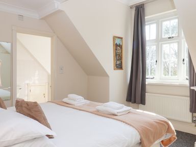 A bedroom with a double bed towels on the bed brown cushions a window with grey curtains and a painting on the wall at Alston Hall in Battisborough Cross