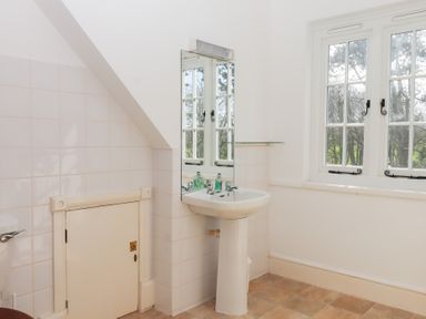 A bathroom with a pedestal sink a mirror and a small door under a slanted ceiling at Alston Hall in Battisborough Cross