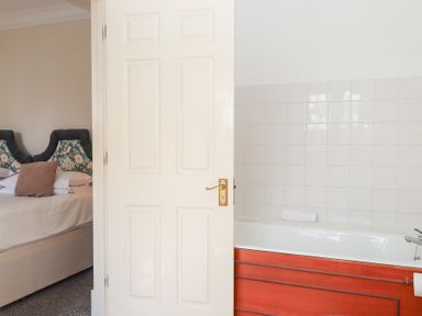 A partially open door showing a bedroom with a bed and a bathroom with a bathtub at Alston Hall in Battisborough Cross