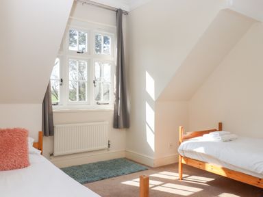 A bedroom with two single wooden beds next to a window with grey curtains and a blue rug on the floor at Alston Hall in Battisborough Cross