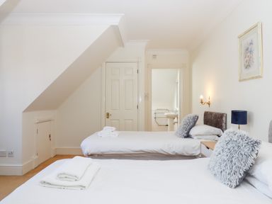 A bedroom with two single beds white walls a door and an ensuite bathroom at Alston Hall in Battisborough Cross