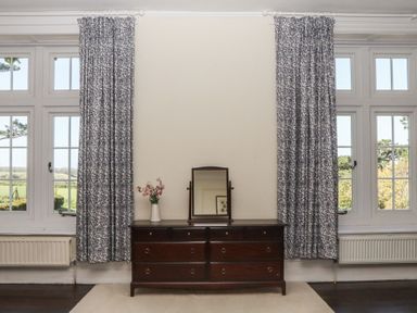 A dresser with a mirror and flower vase near windows at Alston Hall near Mothecombe Beach