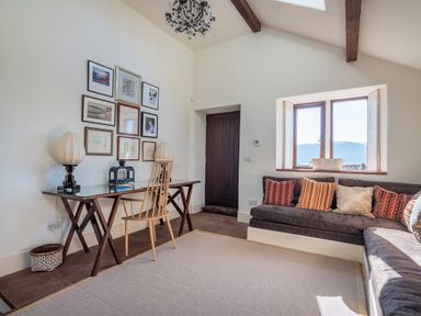 A room with a wooden desk and chair, a sofa with patterned cushions, framed pictures on the wall, and a window with a view at Bank Barn Wreay in Watermillock