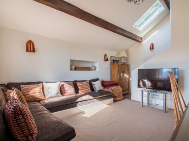 A living room with a sectional sofa with cushions a wooden cabinet a television on a glass stand and a skylight at Bank Barn Wreay in Watermillock