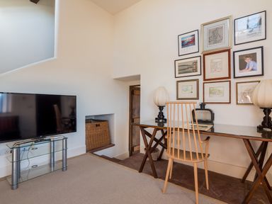 A room with a glass desk and wooden chair two table lamps a tv on a glass stand and framed pictures on the wall at Bank Barn Wreay Watermillock