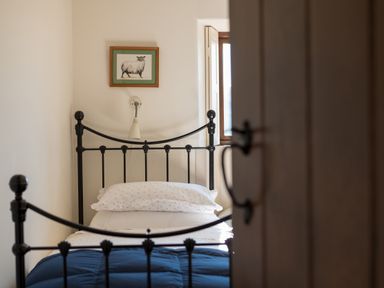 A bedroom with a black metal bed frame a bed with white pillows and a blue blanket a small window and a framed picture of a sheep on the wall at Bank Barn  Wreay