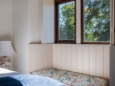 A bedroom corner with a window seat cushion and a lamp on a bedside table at Bank Barn Wreay in Watermillock