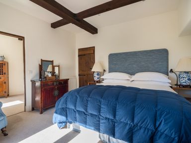 A bedroom with a blue bedspread wooden furniture and blue and white lamps at Bank Barn Wreay in Watermillock