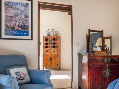 A blue armchair with a pillow by a framed artwork and wooden furniture with decorative items in a room at Bank Barn Wreay Watermillock