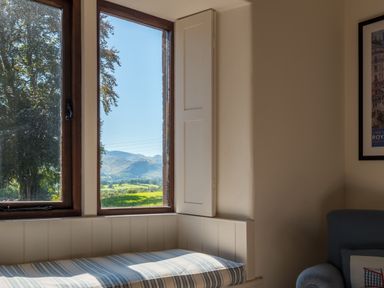 A window seat with a striped cushion and a view of trees and mountains at Bank Barn Wreay Watermillock