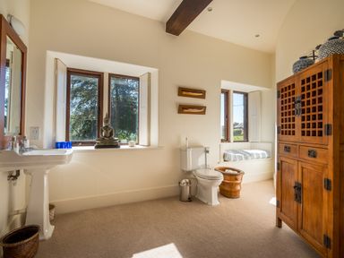 A bathroom with a pedestal sink toilet wooden cabinet and a window seat at Bank Barn Wreay Watermillock
