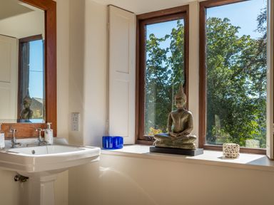 A bathroom sink with a mirror and a Buddha statue on the windowsill at Bank Barn Wreay Watermillock