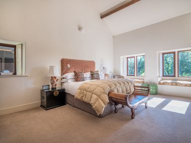A bedroom with a bed and padded headboard bedside tables with lamps and window seats at Bank Barn Wreay in Watermillock
