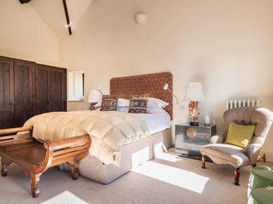 A bedroom with a bed with patterned pillows and a wooden bench at the foot of the bed and an armchair with a green cushion near a black bedside table with lamps Bank Barn Wreay Watermillock