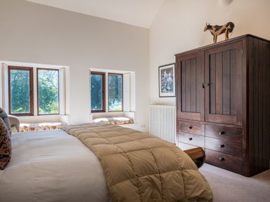 A bedroom with a bed a wooden wardrobe two windows with seating and a framed picture on the wall at Bank Barn Wreay Watermillock