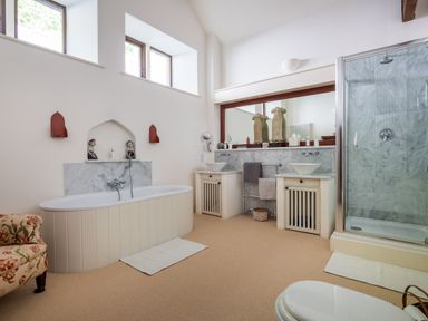 A bathroom with a bathtub double sinks a shower and a floral armchair at Bank Barn Wreay in Watermillock