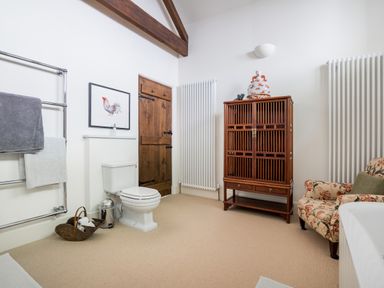 A bathroom with a toilet wooden cabinet floral armchair and a towel rack at Bank Barn Wreay in Watermillock