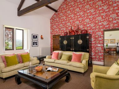 A living room with two sofas a green armchair a black coffee table and a red patterned wallpaper at Bank Barn Wreay in Watermillock