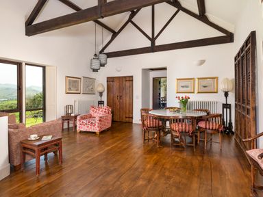 A dining room with a round table and chairs wooden beams and armchairs near windows at Bank Barn in Wreay Watermillock