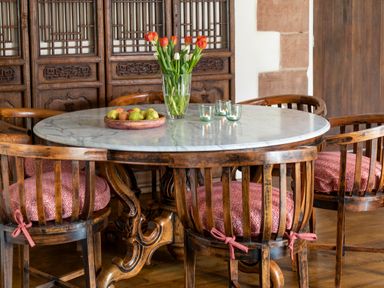 A round dining table with a marble top and wooden base surrounded by wooden chairs with red cushions and a vase of flowers on the table at Bank Barn Wreay in Watermillock