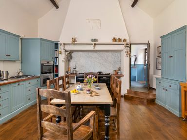 A kitchen with wooden dining table and chairs blue cabinets and a marble backsplash at Bank Barn Wreay Watermillock