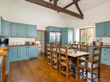 A kitchen with wooden floor blue cabinets a dining table with chairs and flowers on table at Bank Barn Wreay in Watermillock