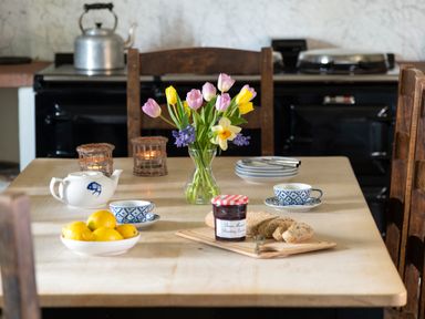 A wooden dining table with a vase of flowers teapot lemons bread jam cups and plates at Bank Barn Wreay Watermillock