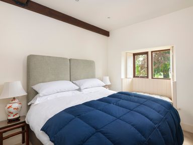 A bedroom with a double bed white pillows a blue quilt two bedside tables with lamps and a window seat by Bank Barn Wreay in Watermillock