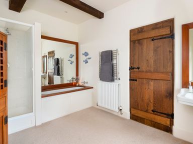 A bathroom with a wooden door a bathtub with a wooden frame a shower and a towel rack at Bank Barn Wreay Watermillock