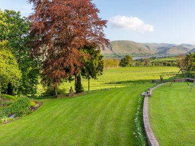 A garden with trees lawn sculpture and swing set overlooking hills and water at Bank Barn Wreay in Watermillock